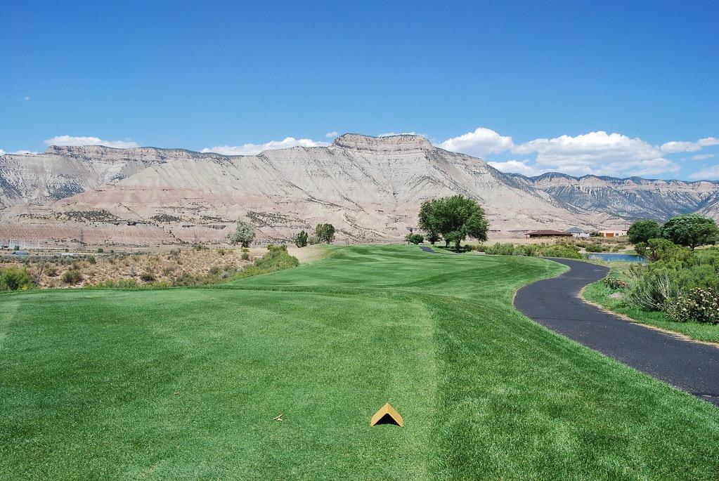 Sunny golf course with green fairway, cart path, and distant arid mountains.