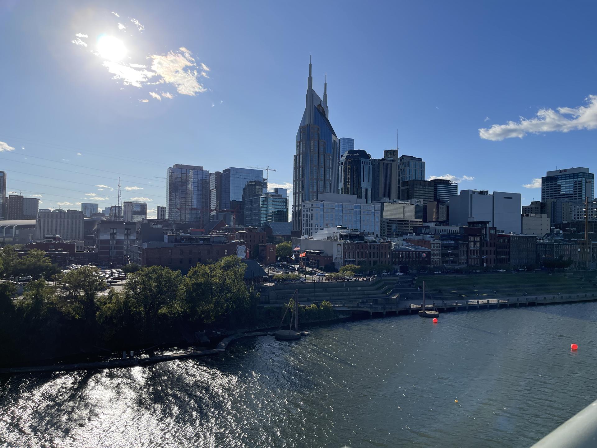 Sunny city skyline with a spired building, river, and bright sun.