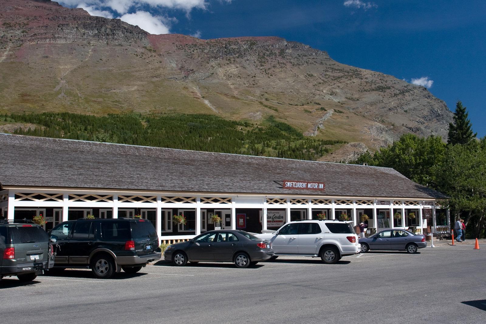 A long building with parked cars sits before a large, rocky mountain.