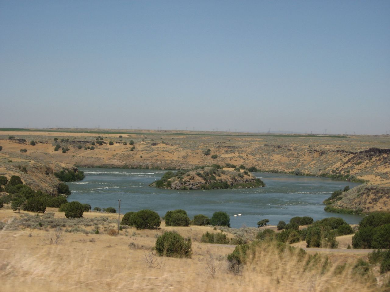 Wide river with an island, surrounded by dry, rocky hills under a clear sky. - Snake River Trail