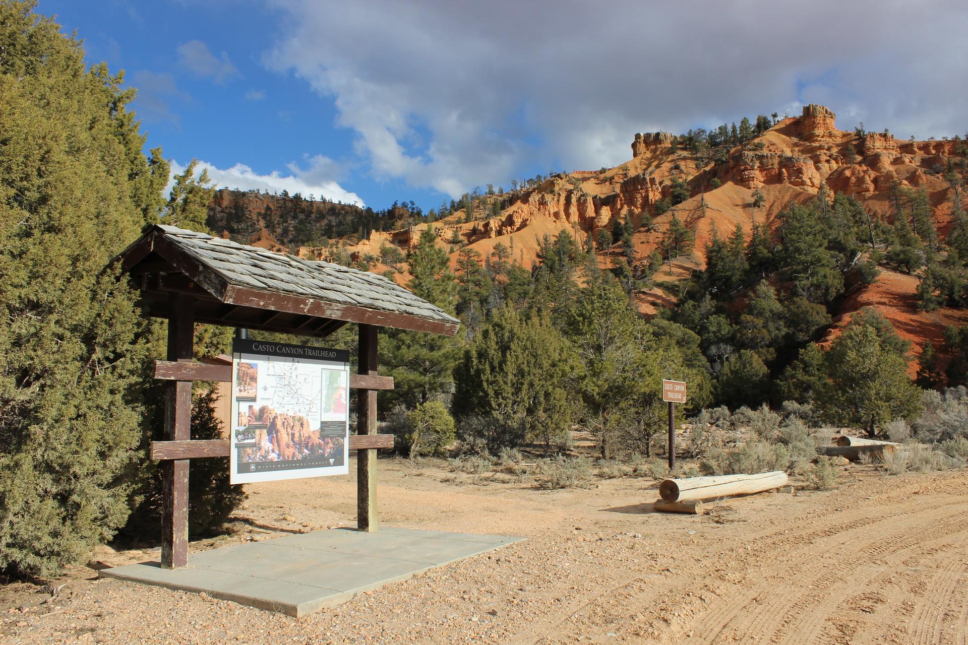 Wooden information kiosk on a dirt path, with red hills and trees.