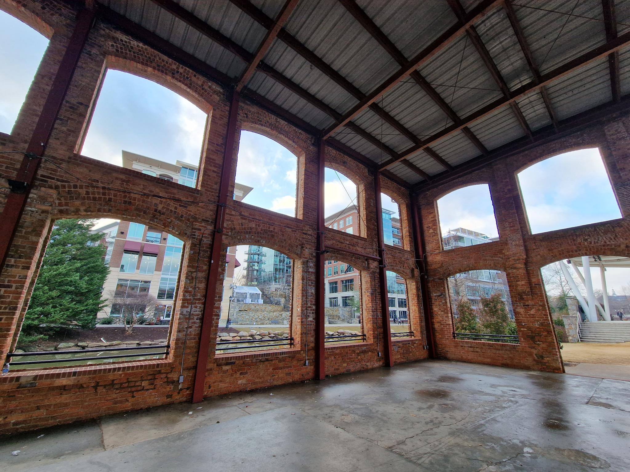 Empty brick building interior with arched windows overlooking modern buildings and trees.