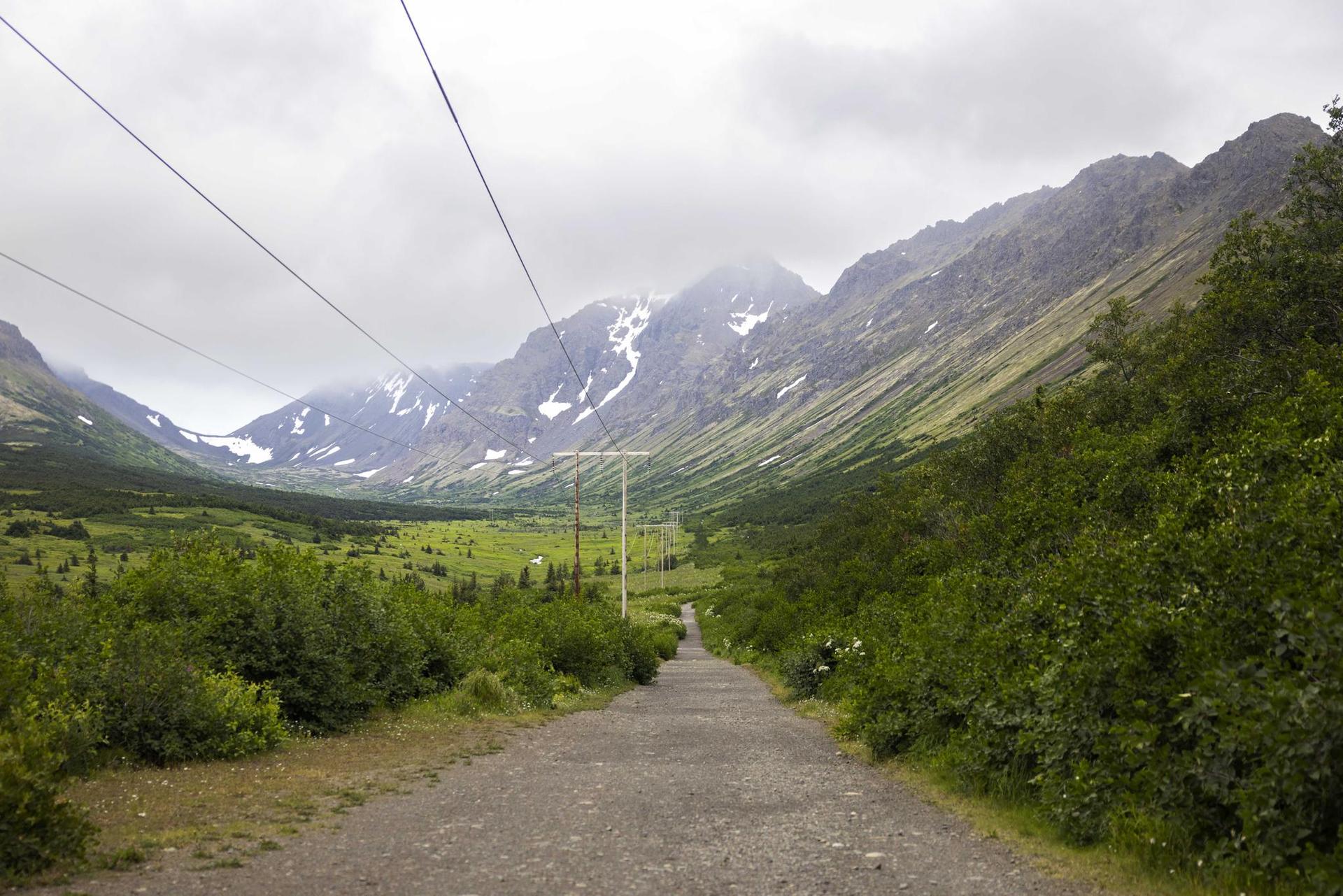 Gravel road leading through a green mountain valley with power lines overhead.