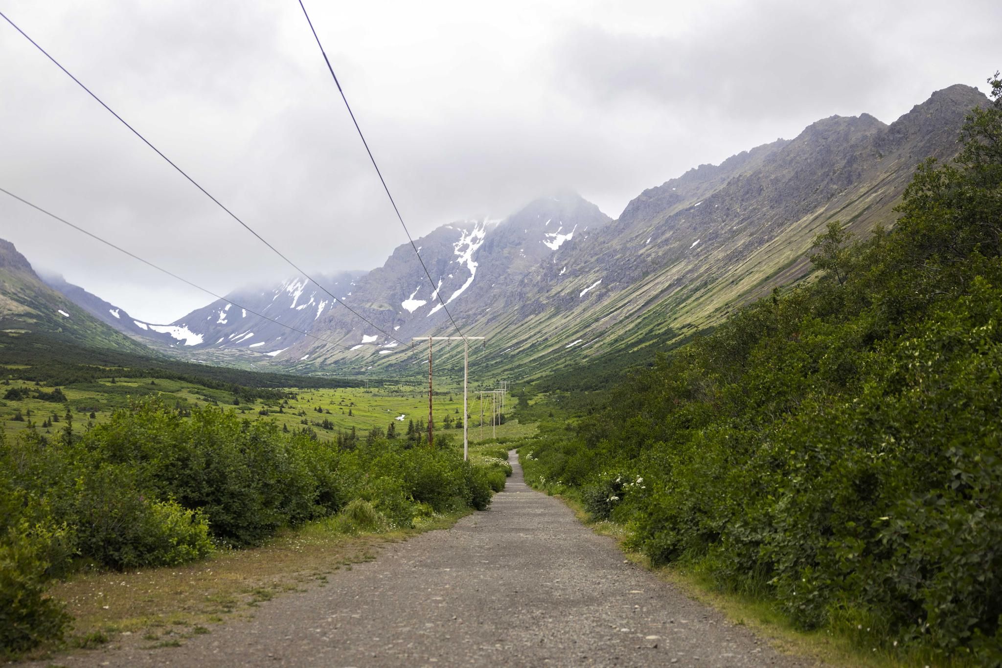 Gravel road leading through a green mountain valley with power lines overhead. - Powerline Pass Trail