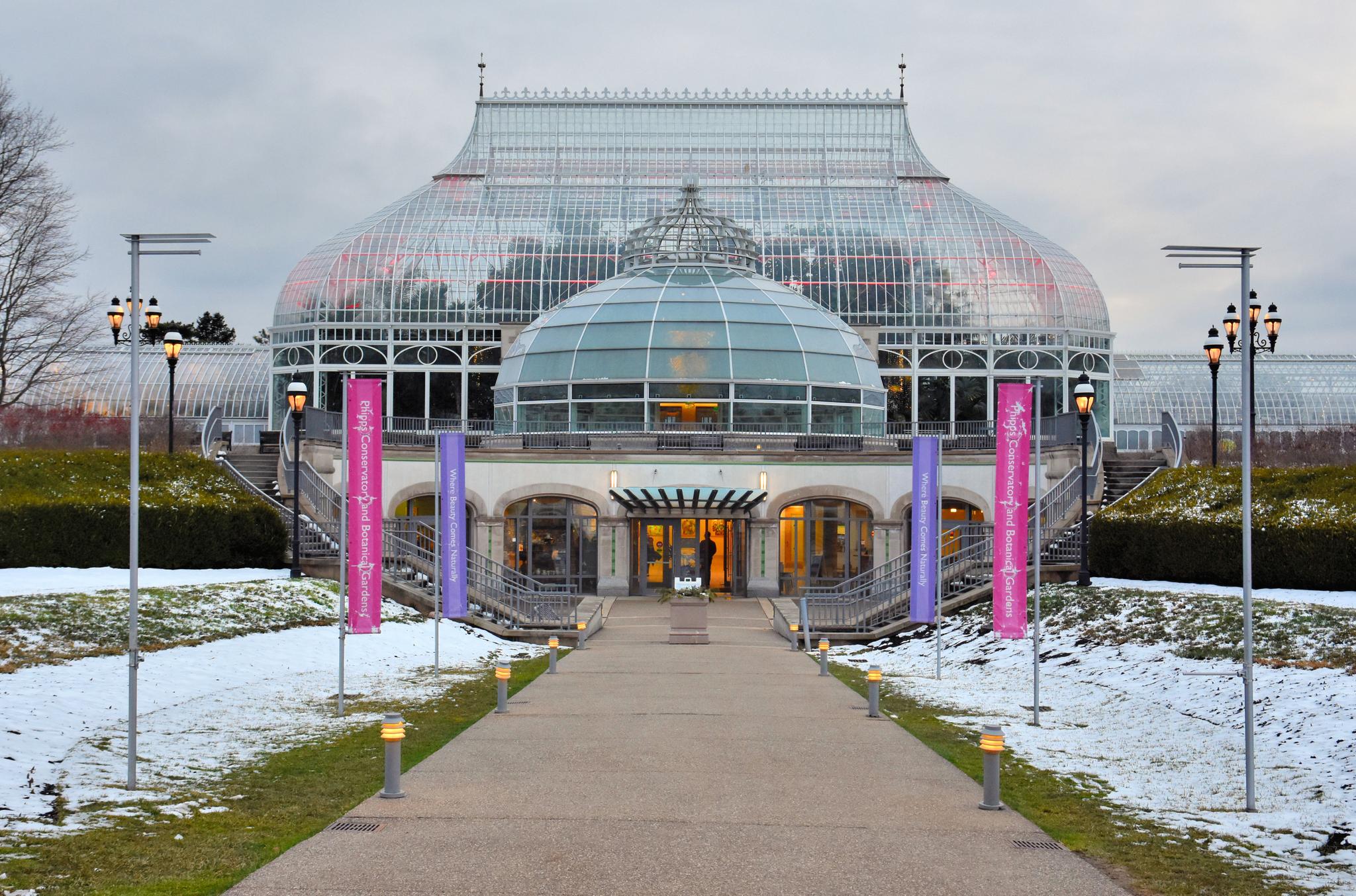 Grand glass conservatory building with snow on the ground under an overcast sky.