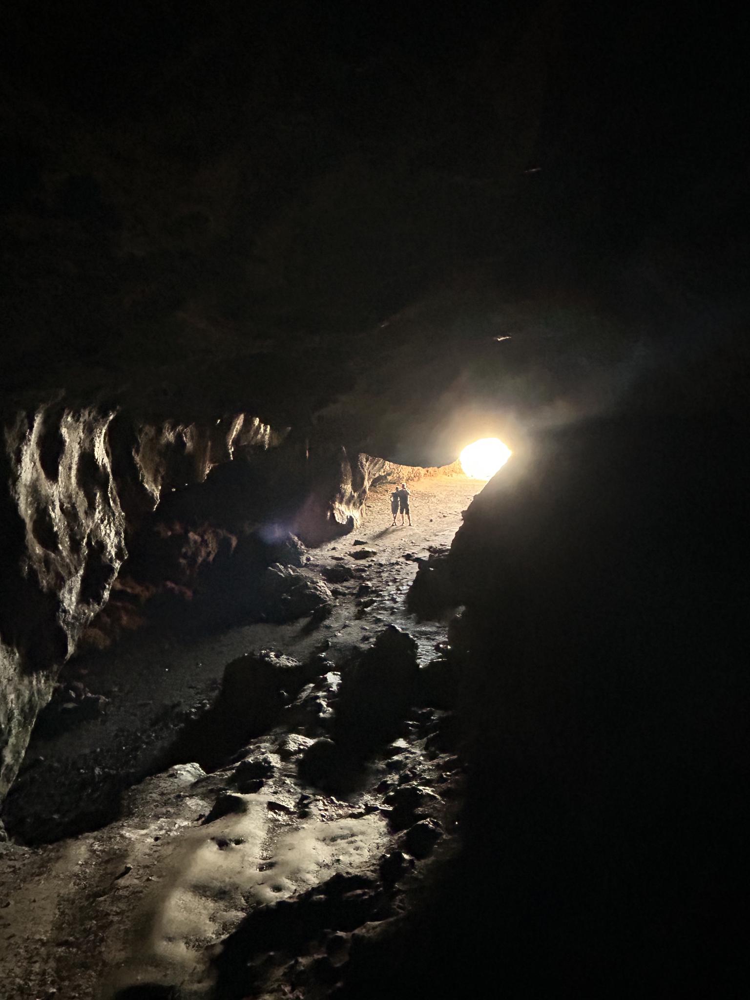 Two people walk towards a bright light in a dark, rocky cave.