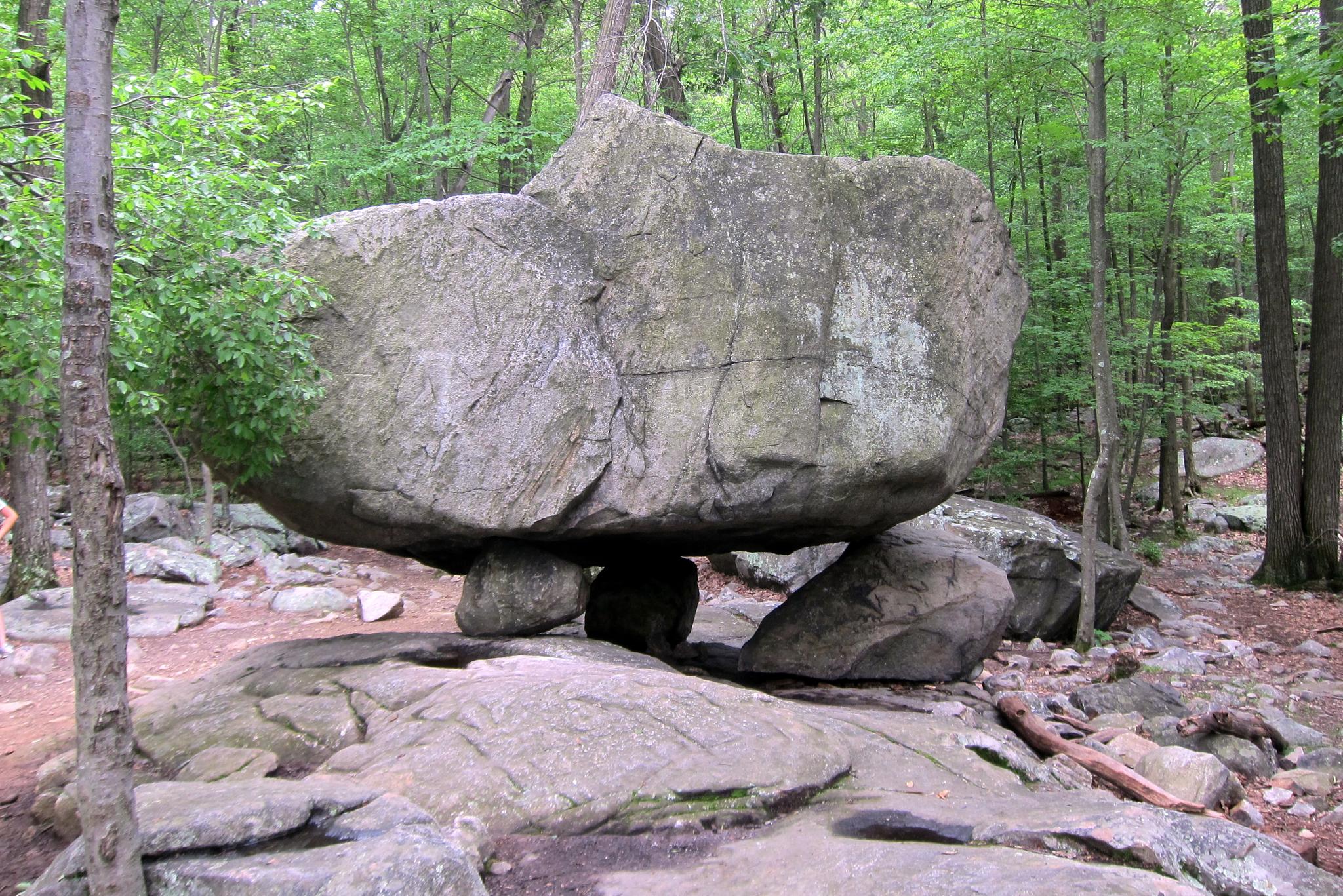 A massive balanced rock formation stands in a lush green forest.