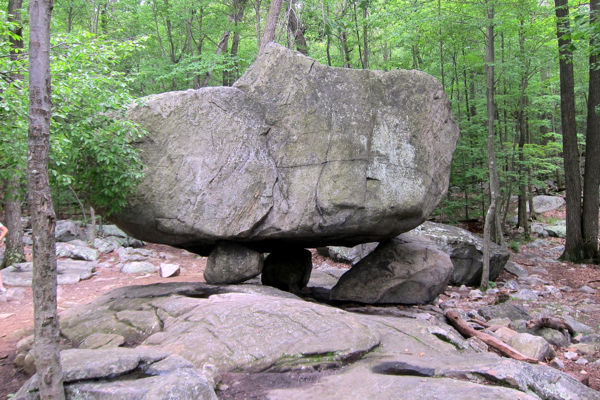 A massive balanced rock formation stands in a lush green forest.