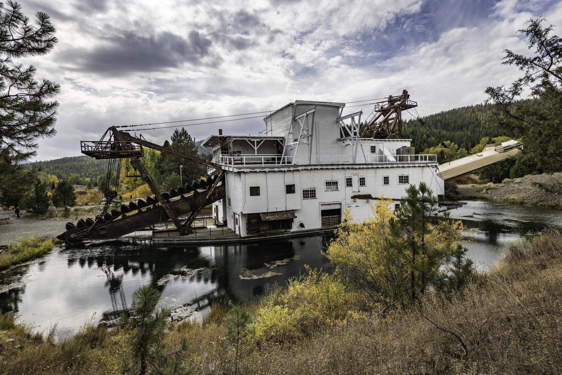 Large white dredge boat on water with dramatic cloudy sky and trees.