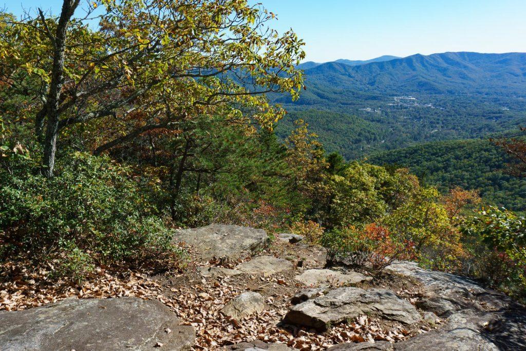 Rocky overlook with autumn leaves, offering a view of a green valley and mountains.