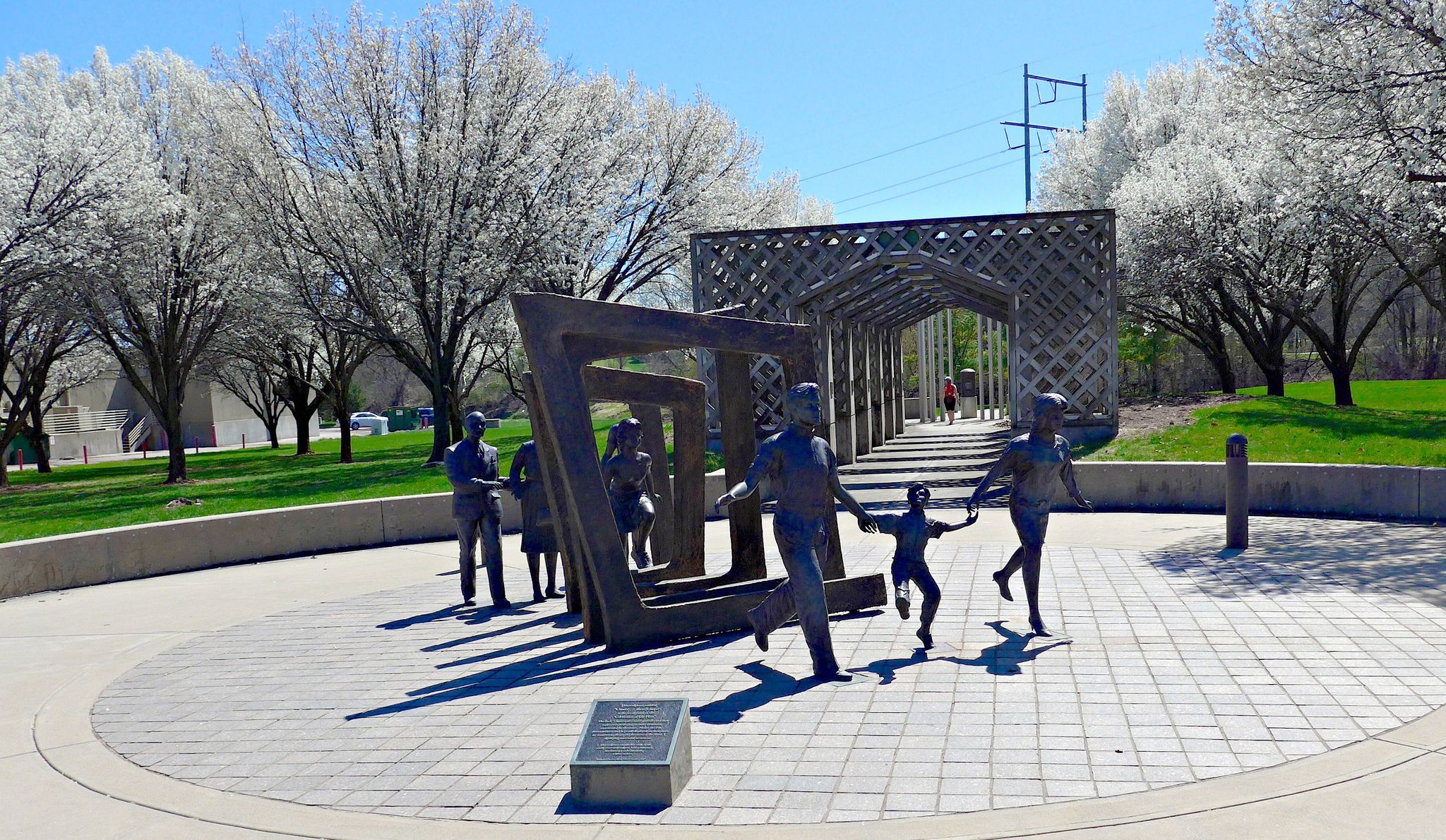 Bronze sculptures of people in a sunny park with white blossoming trees. - Big Papio Trail