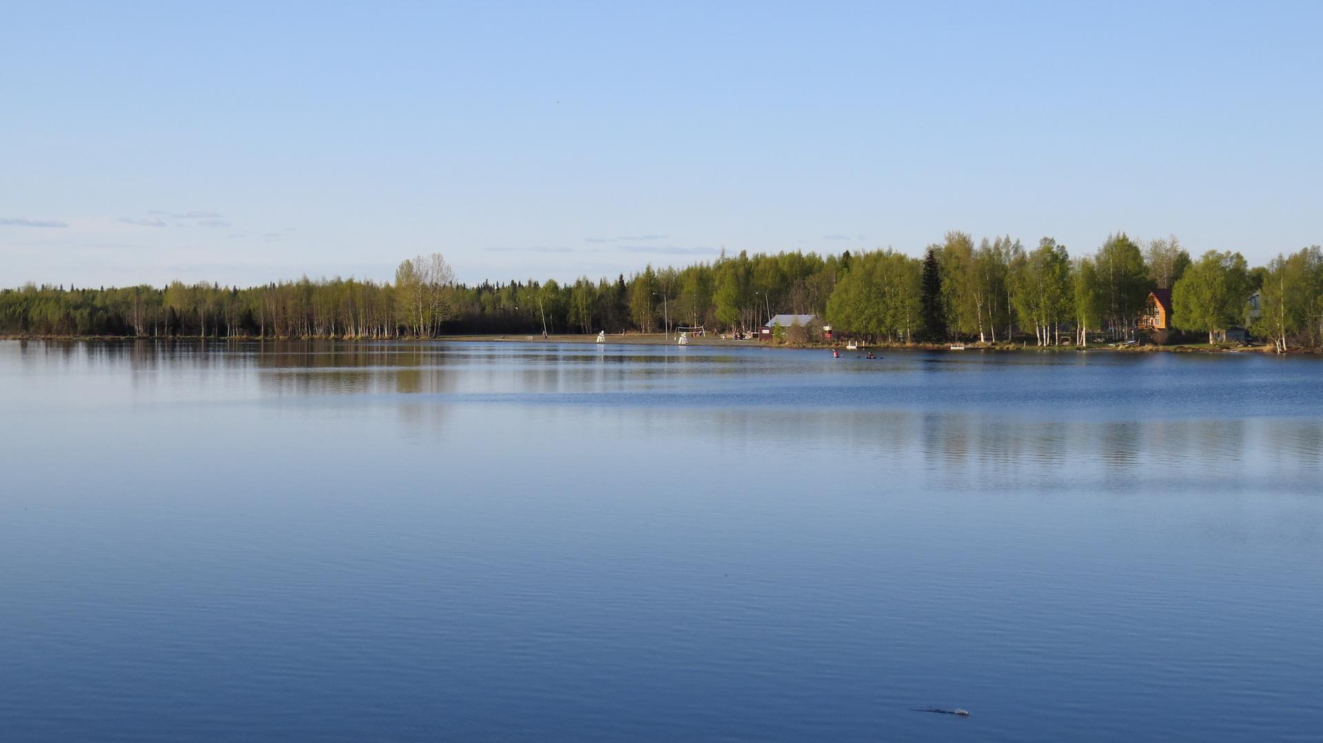 Wide, calm lake reflecting a distant forested shoreline under a clear sky.