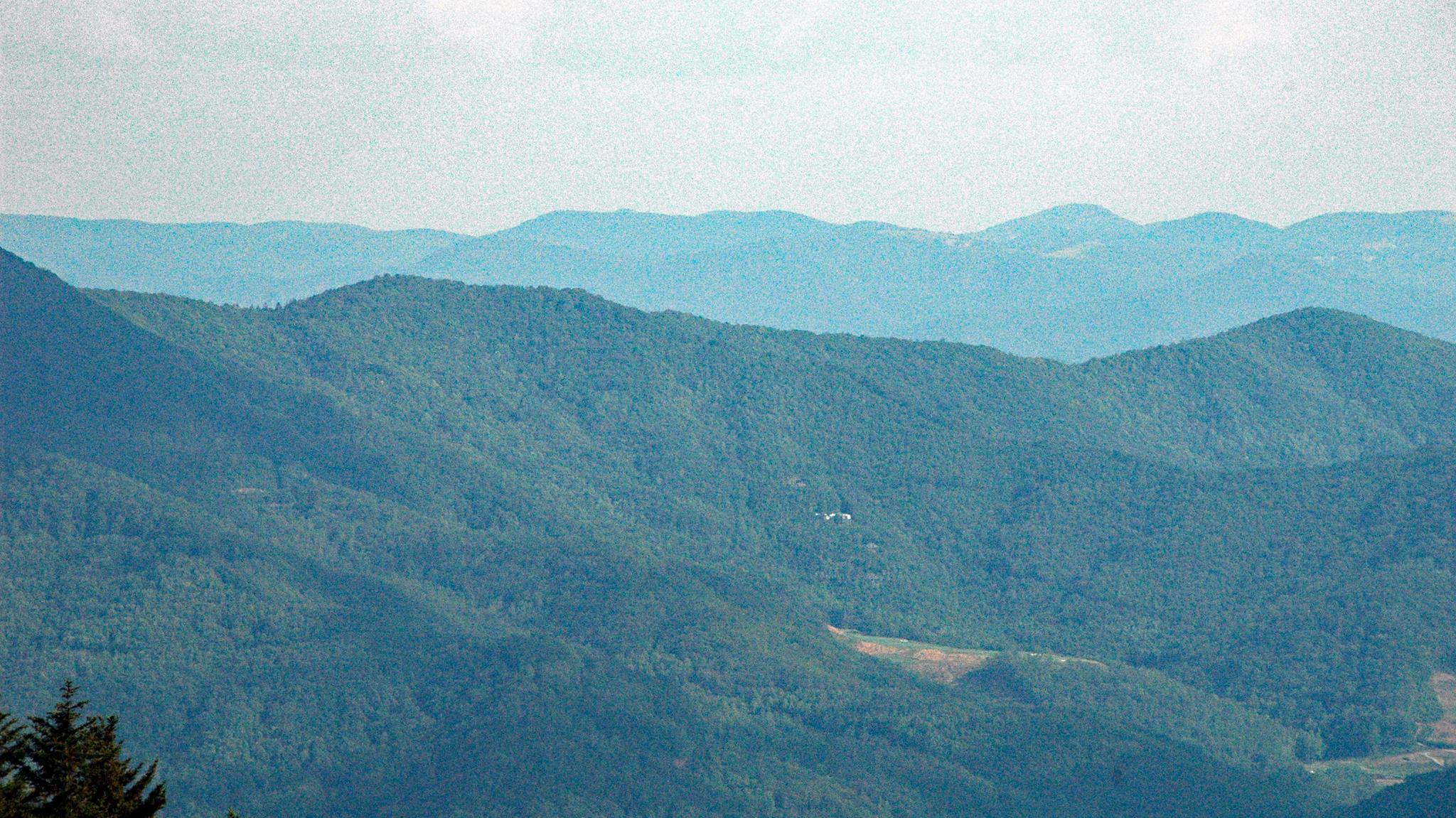 Hazy blue-green forested mountains with faint white objects in the distance.