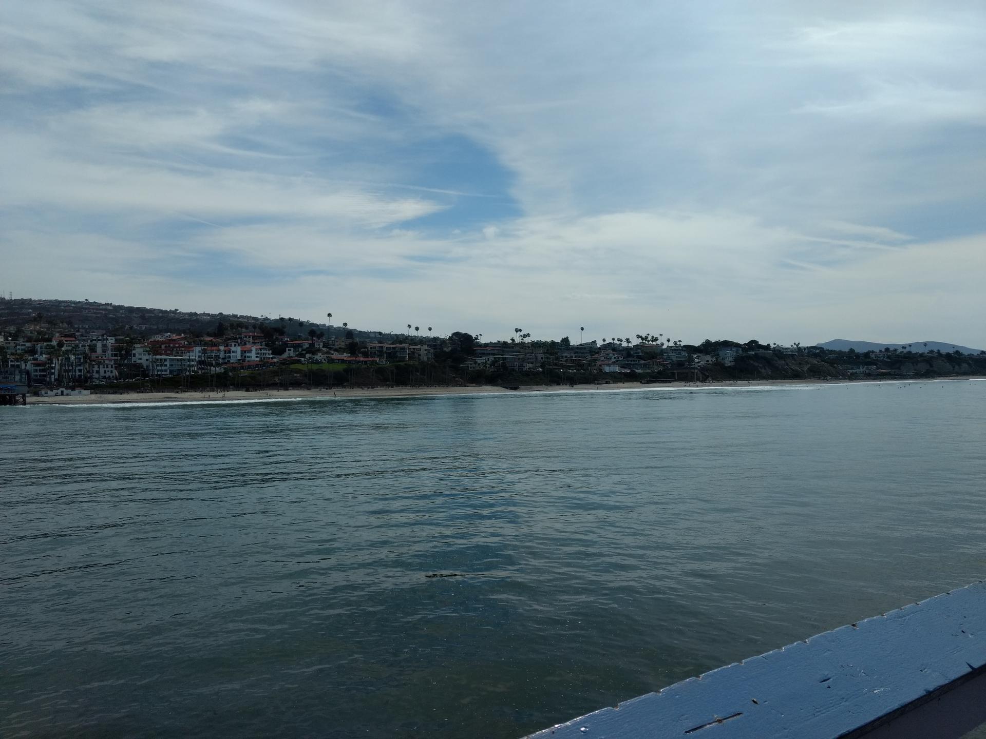 Wide ocean view towards a distant coastline with buildings under cloudy sky.
