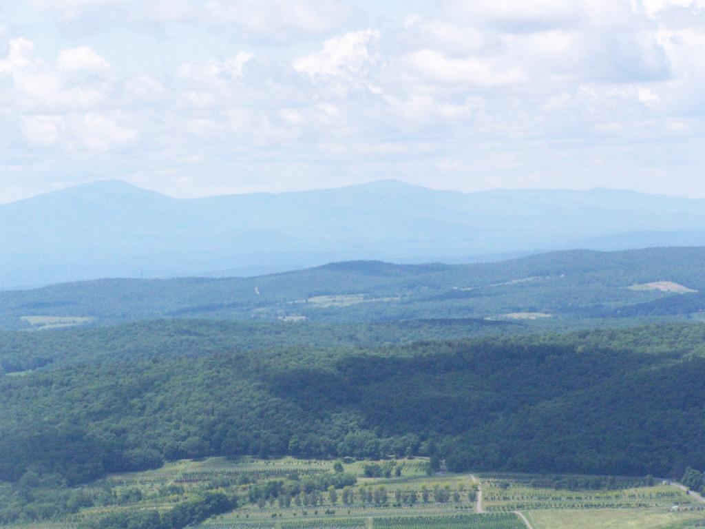 Hazy view of layered blue mountains, green forests, and cultivated fields.