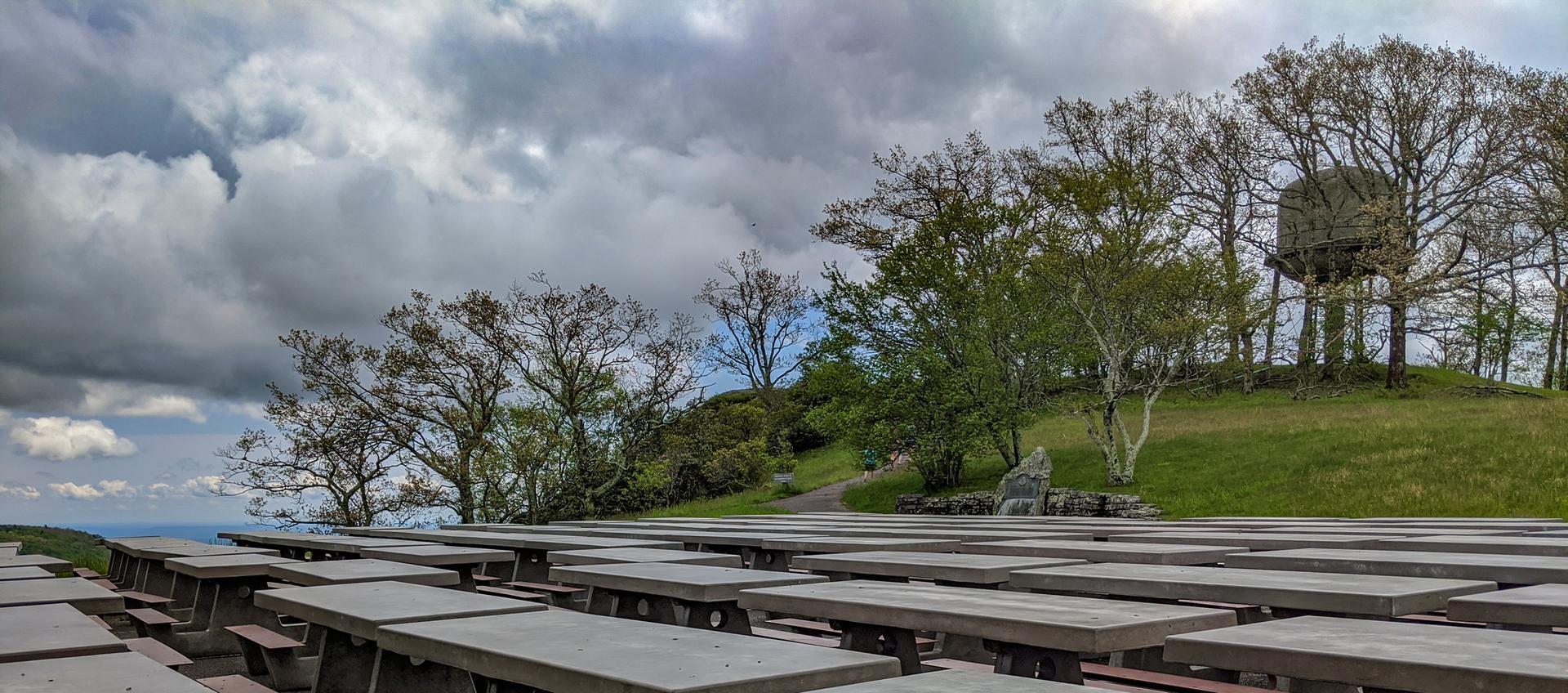 Empty outdoor amphitheater seating on a grassy hill under a cloudy sky.