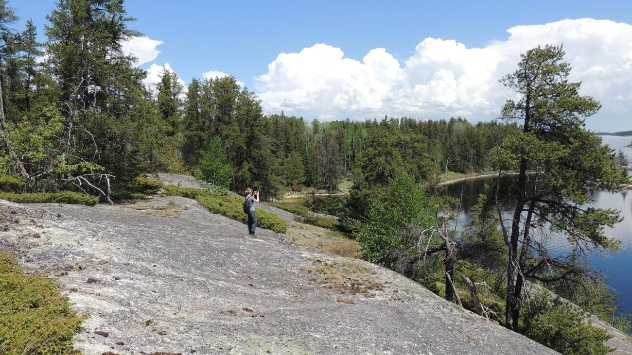 Person on a rocky outcrop overlooking a vast lake and forest.
