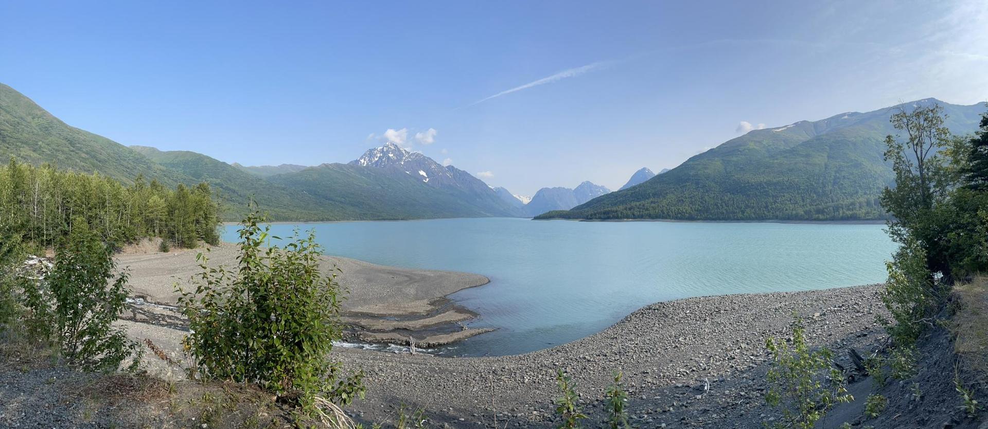 Panoramic view of a glacial lake surrounded by forested mountains under a clear sky.