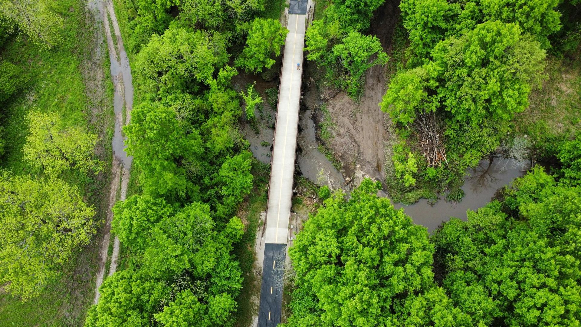 Aerial view of a bridge over a stream surrounded by lush green trees.
