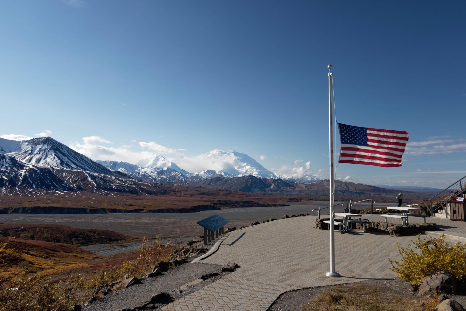 American flag flying proudly over a paved viewing area with snowy mountains.