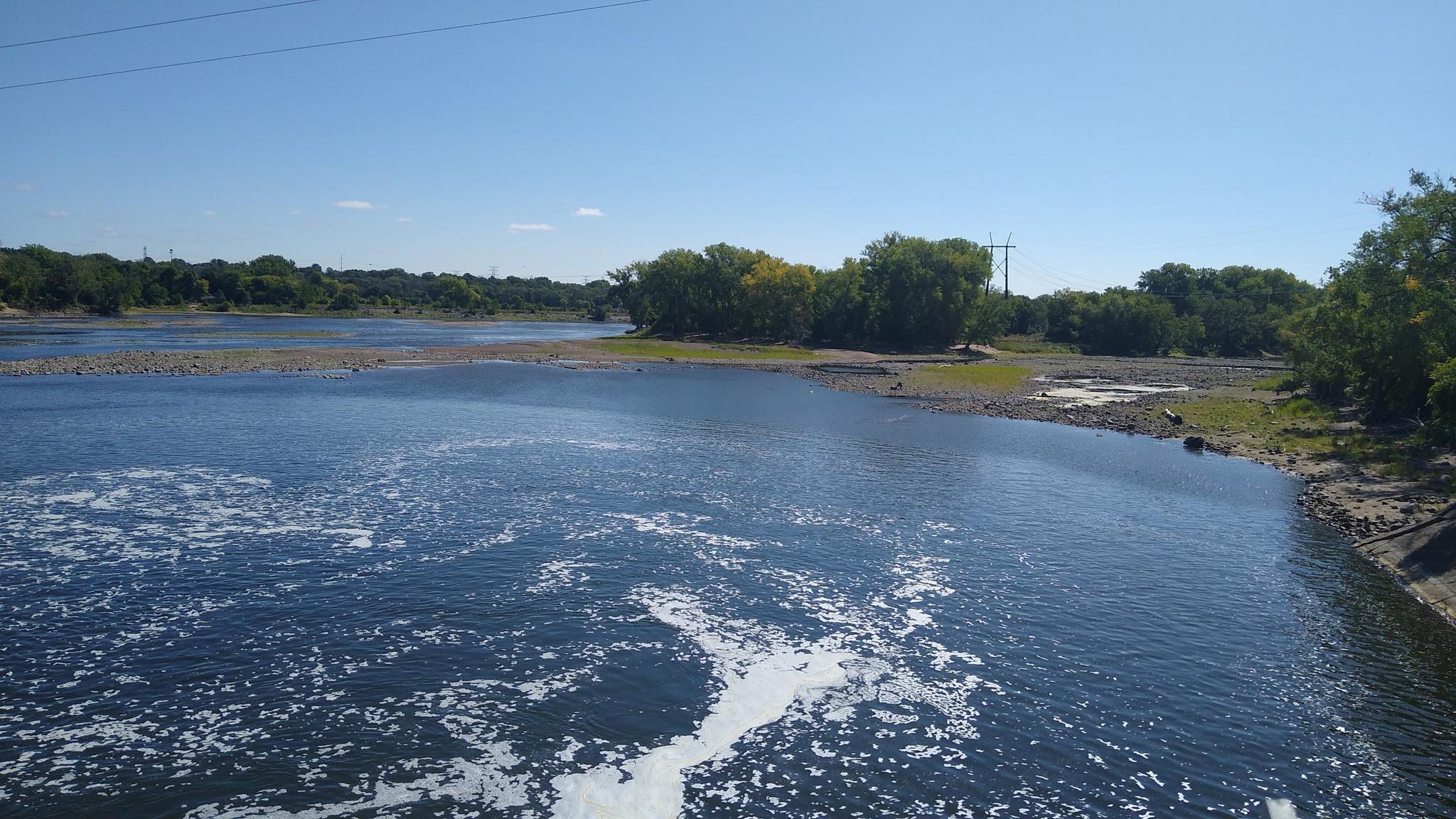 Wide river with foamy water under a bright blue sky.