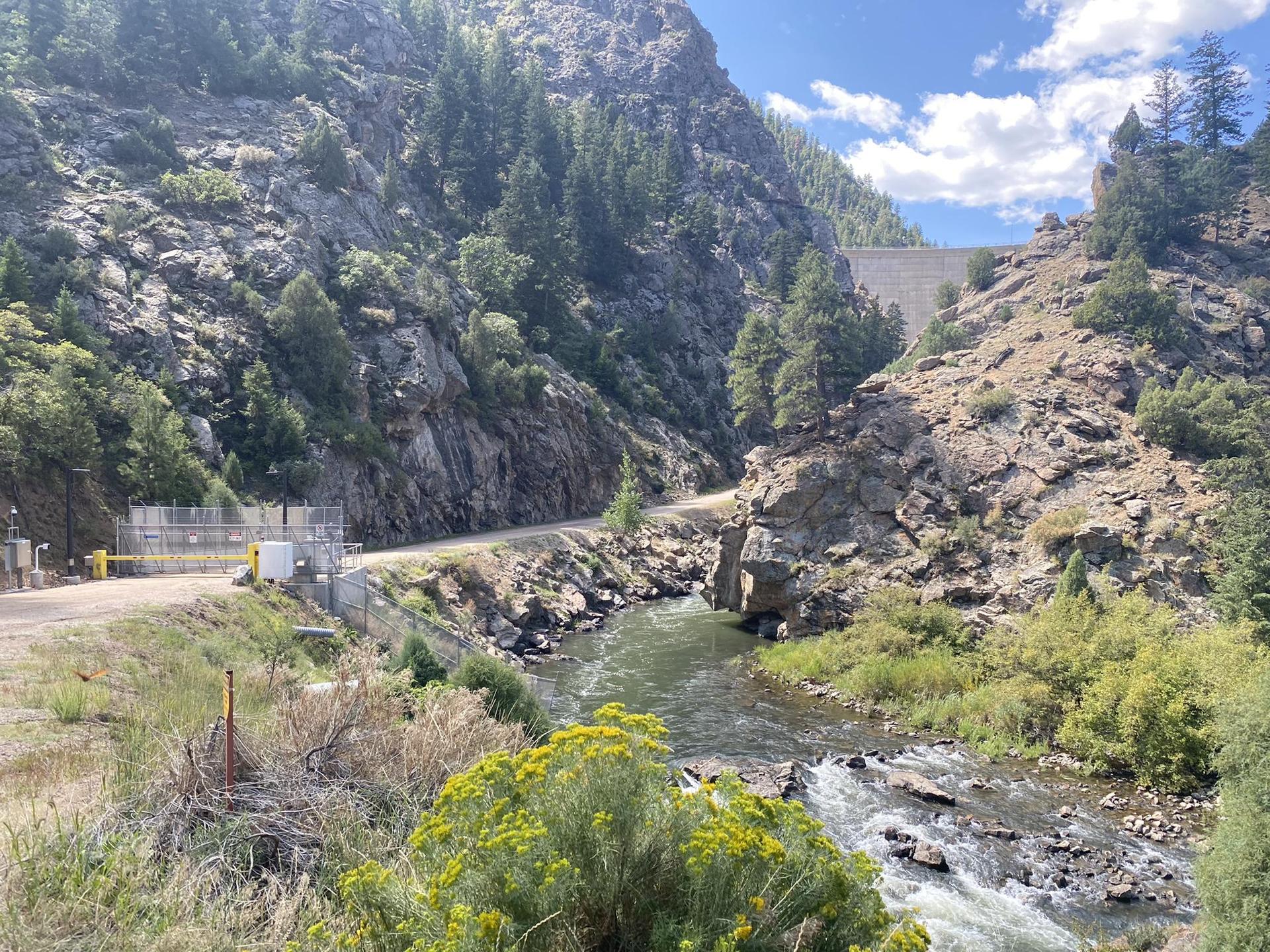 A river flows through a rocky canyon with a road and dam.