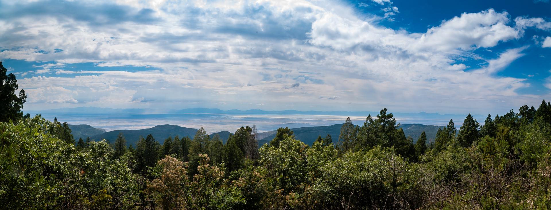 Panoramic view of a vast forested mountain range under a cloudy sky.