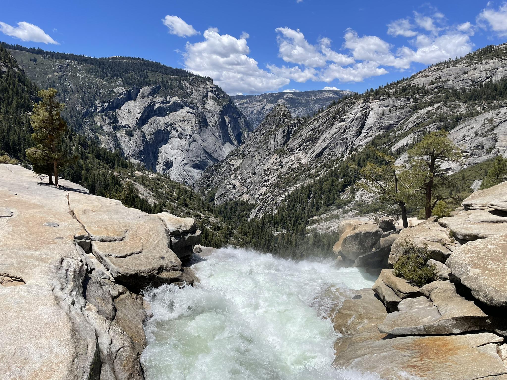 Rushing river over rocks, leading to a deep mountain valley under a bright sky.