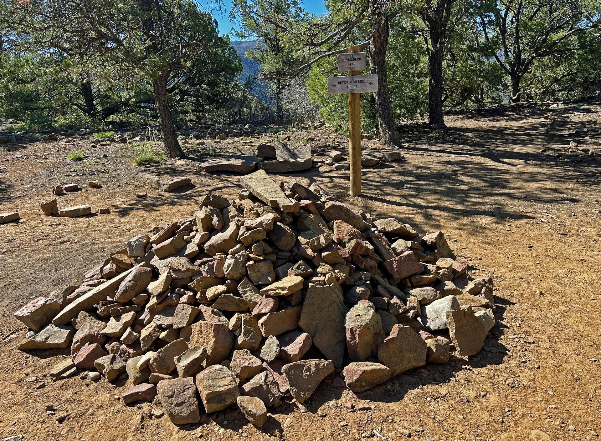 A large rock pile and wooden signpost on a sunny, forested path.