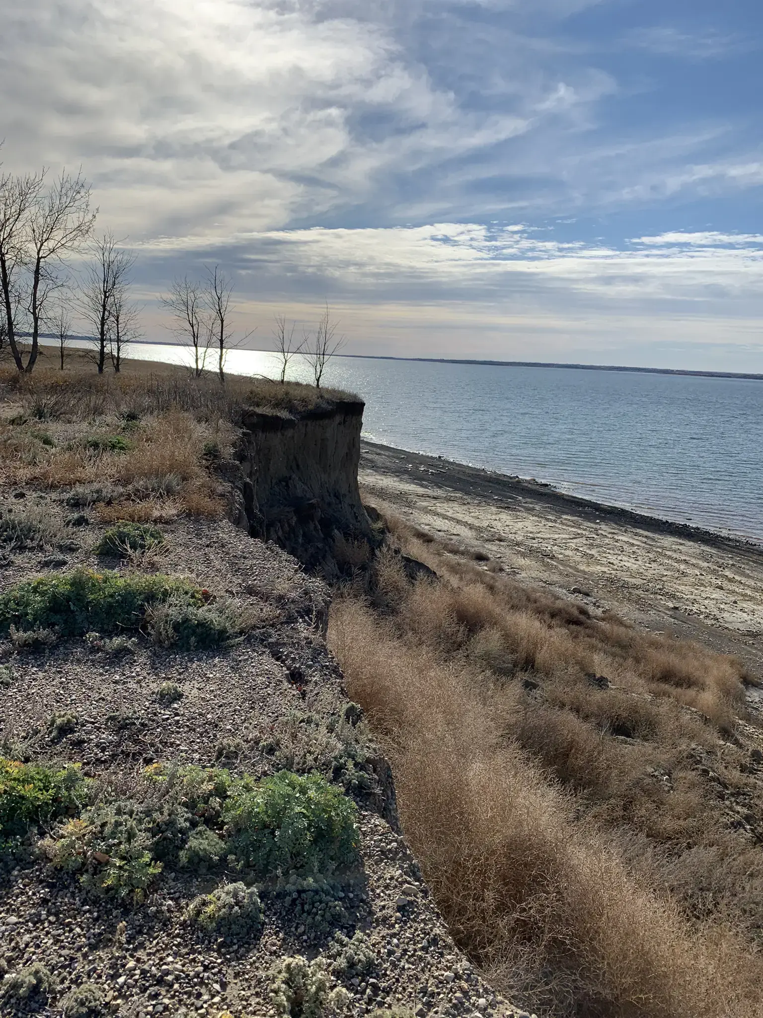 Eroded cliff overlooking a calm lake under a partly cloudy sky.