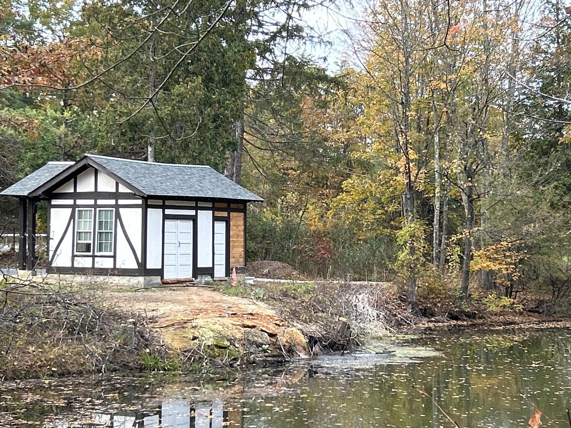 Small white cottage by a calm pond, surrounded by colorful autumn trees.