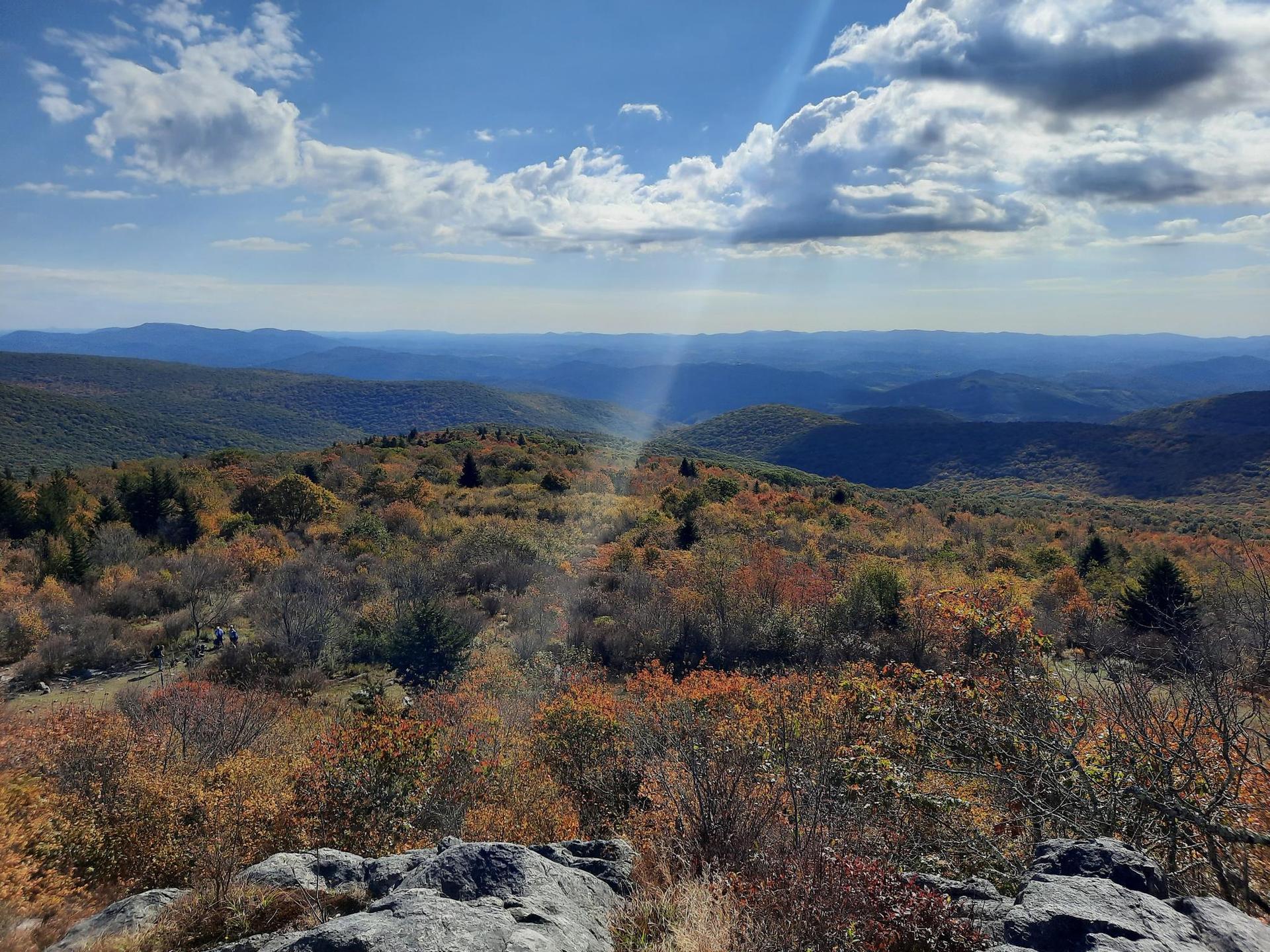 Expansive mountain vista with autumn trees and sun rays through clouds.