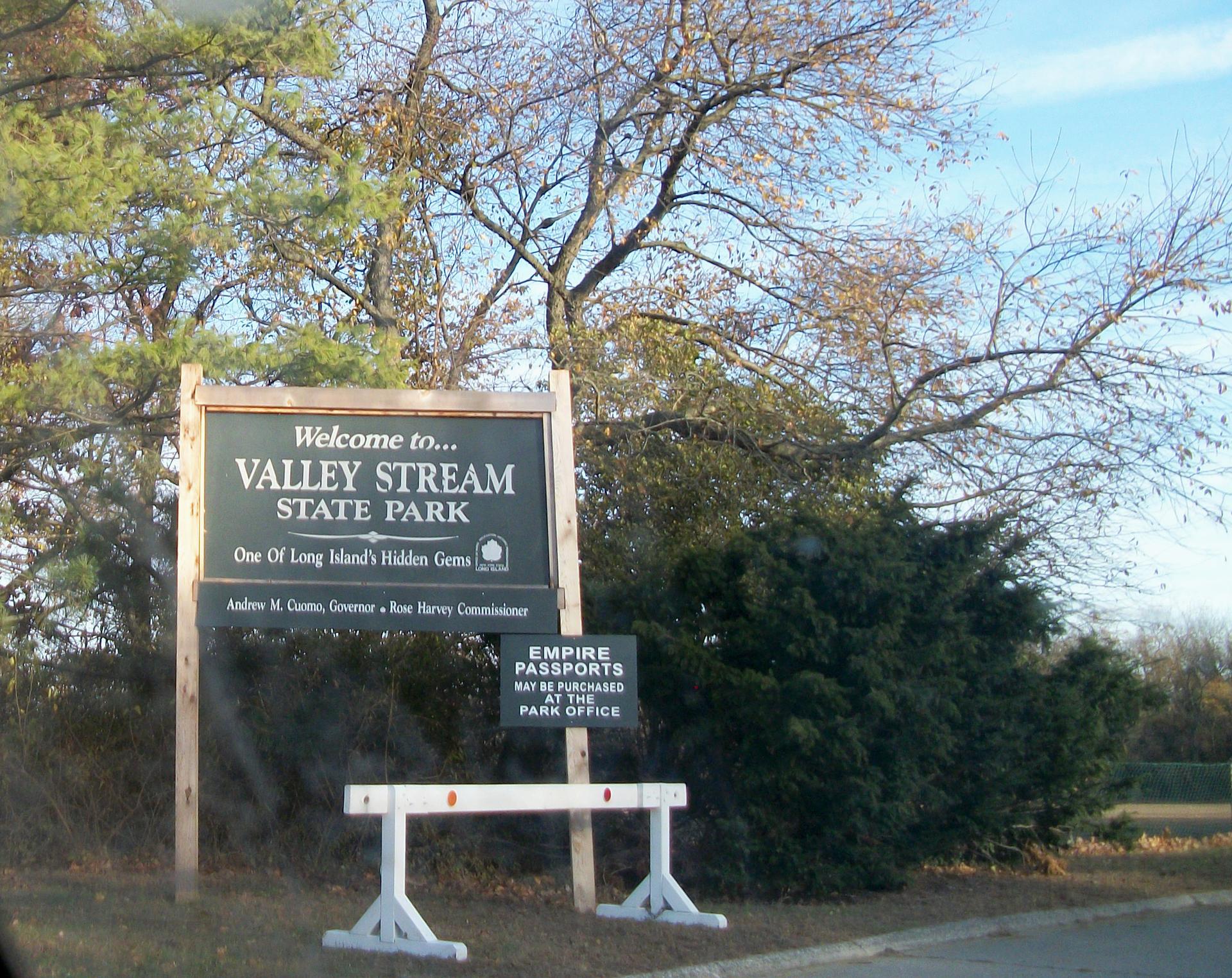 A large welcome sign for a park, surrounded by trees under a bright sky.