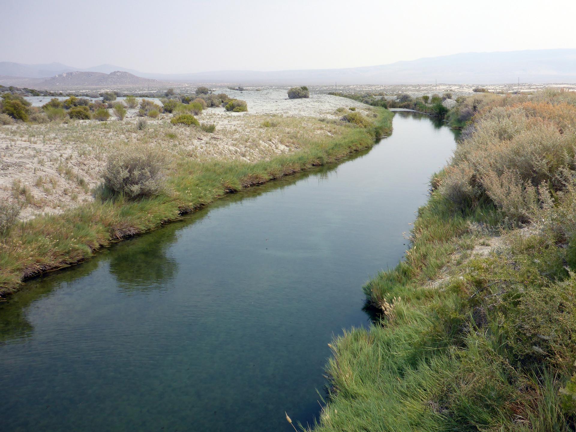 A winding river flows through a dry, grassy landscape under hazy skies.