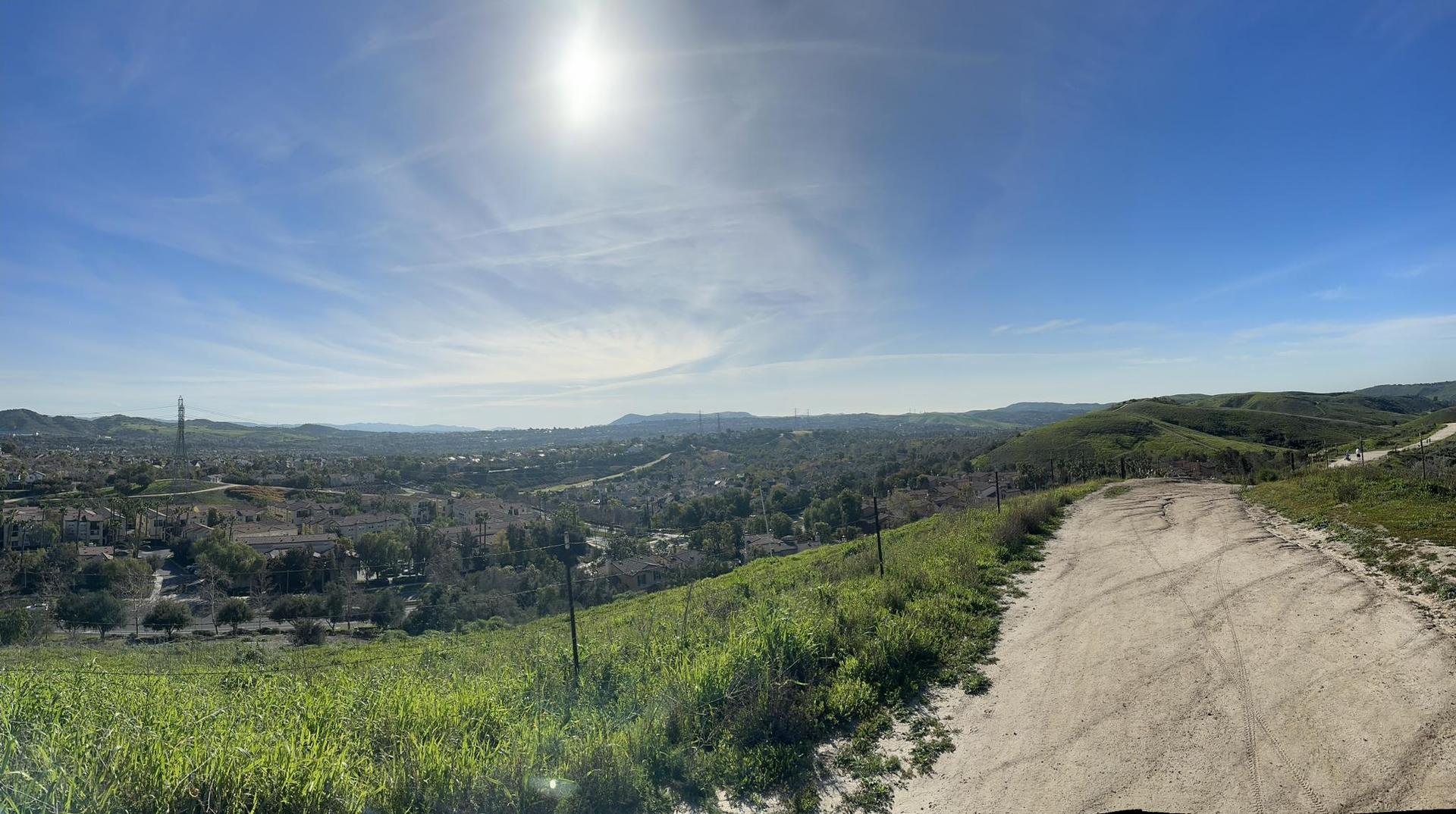 Sunny panoramic view of a dirt path overlooking a distant town and green hills.