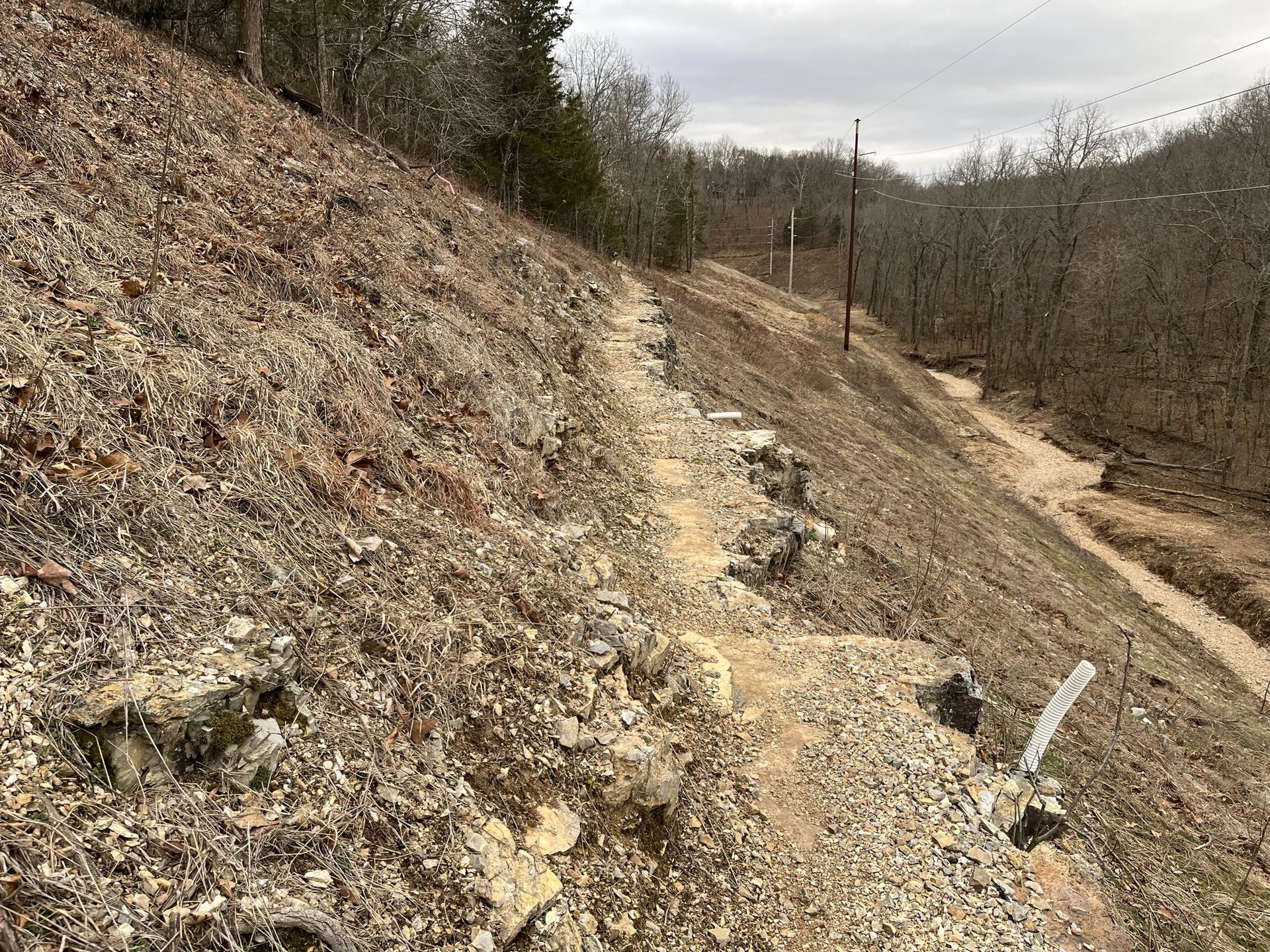 Rocky path on a steep, dry hillside next to a creek.