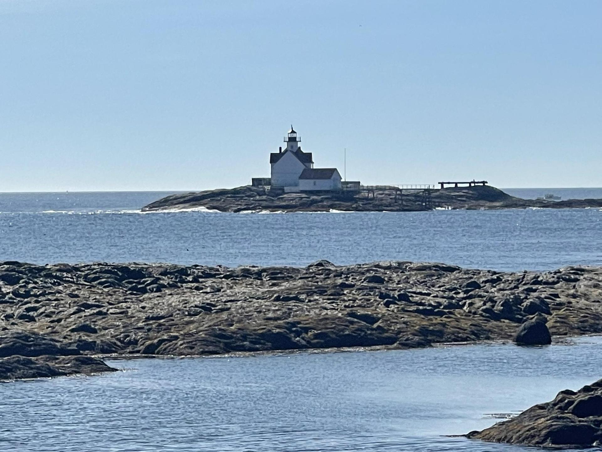 Distant white lighthouse on a rocky island in the bright, clear ocean.
