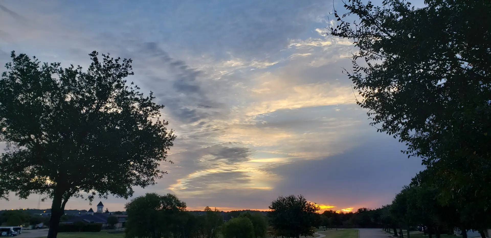Dramatic sunset sky with golden light peeking through clouds and silhouetted trees.