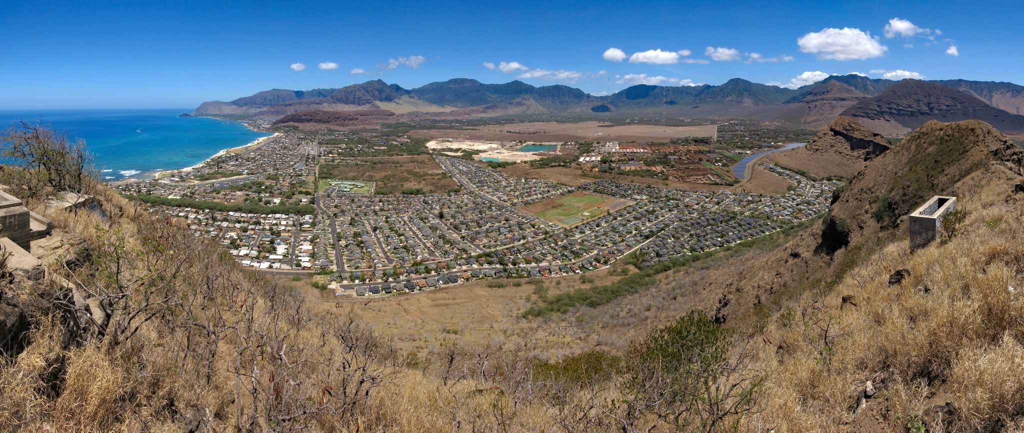 Sunny panoramic view of a coastal town, dry hills, and distant mountains. - Kolekole Pass Loop
