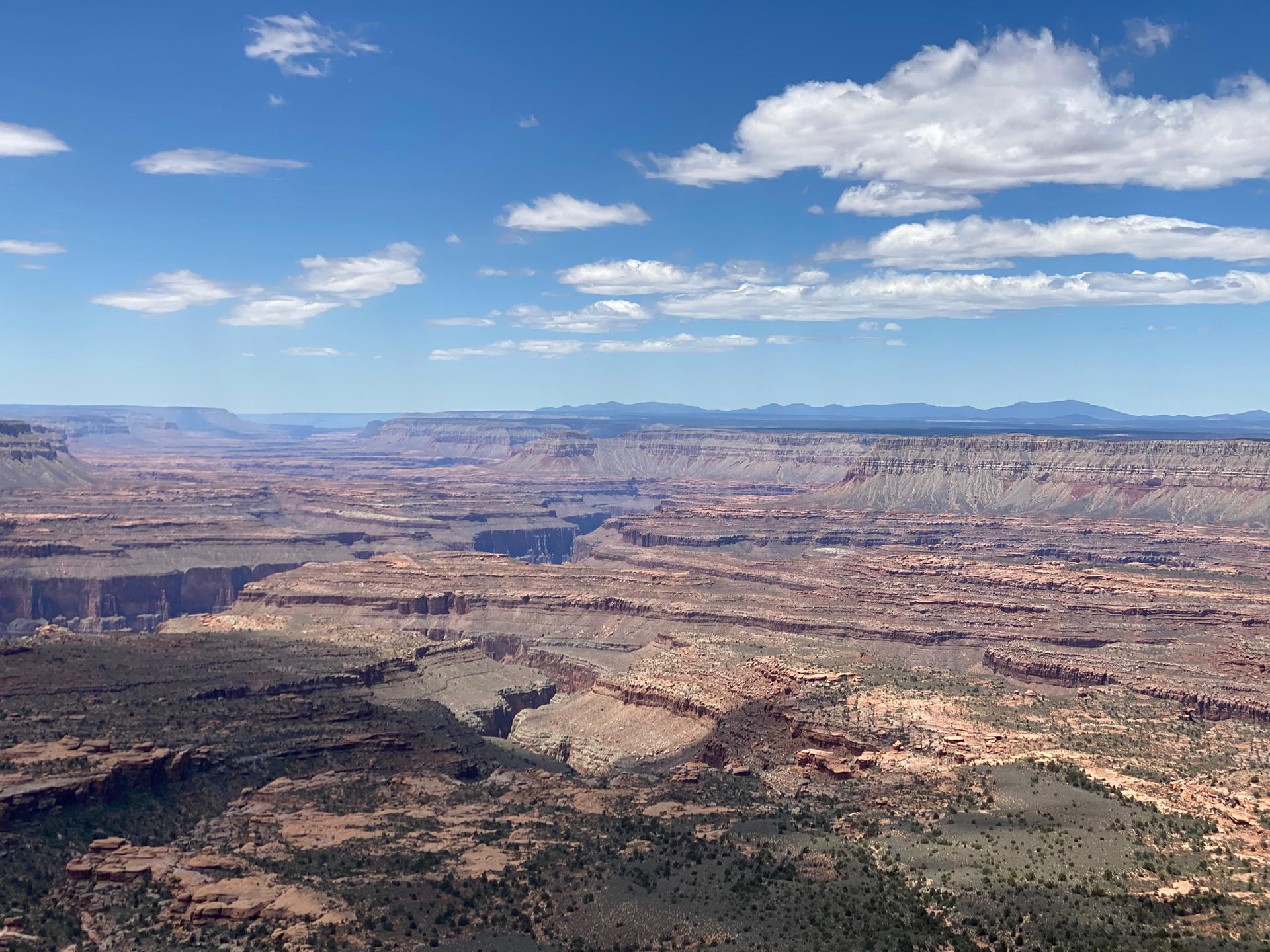 Expansive aerial view of a layered, arid canyon system under a blue sky.