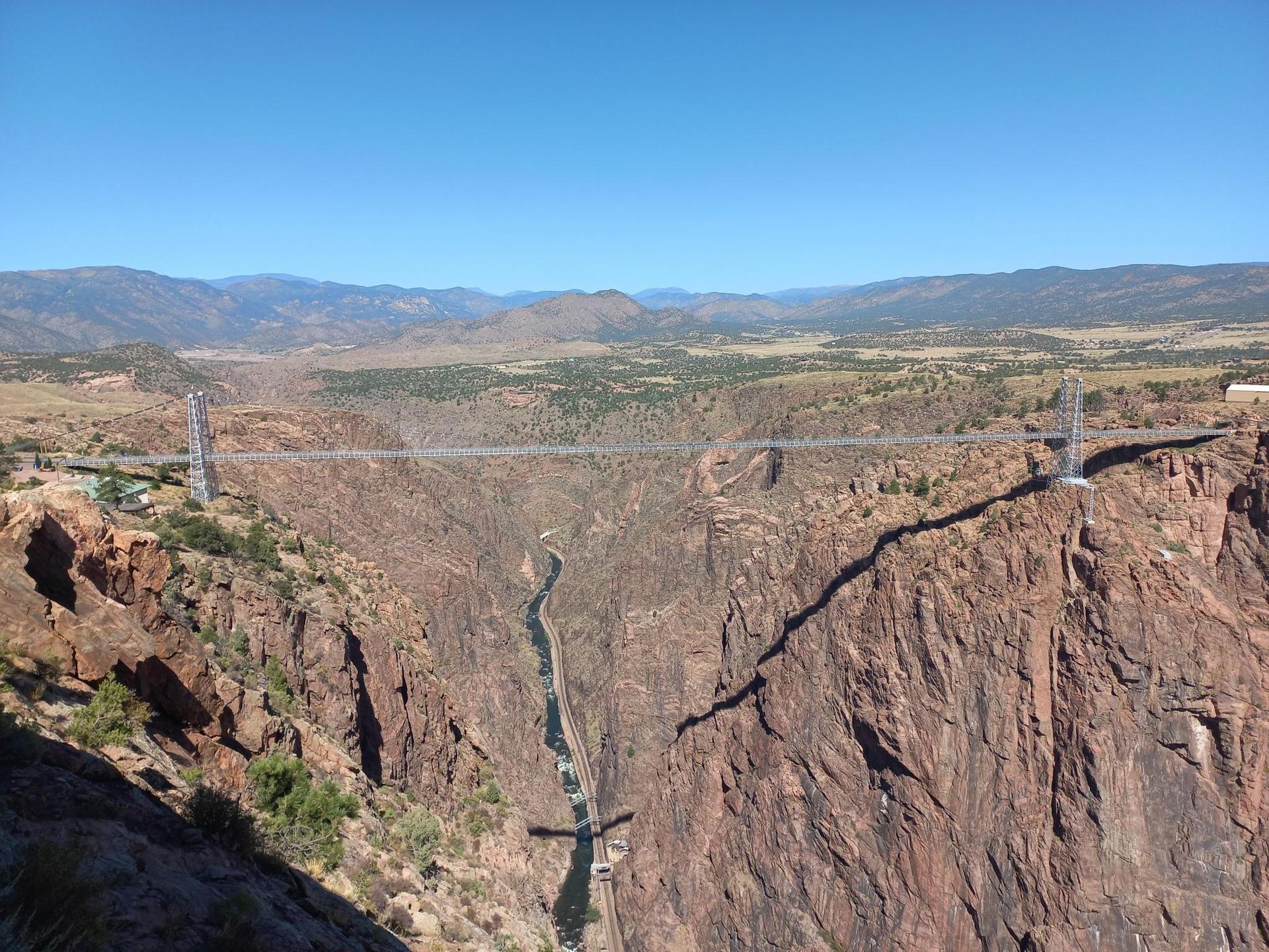 Panoramic view of a suspension bridge spanning a vast, rocky canyon, sunny.