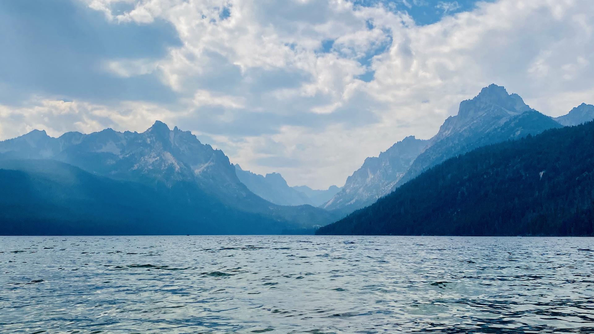 A vast lake with distant, hazy mountains under a dramatic cloudy sky.