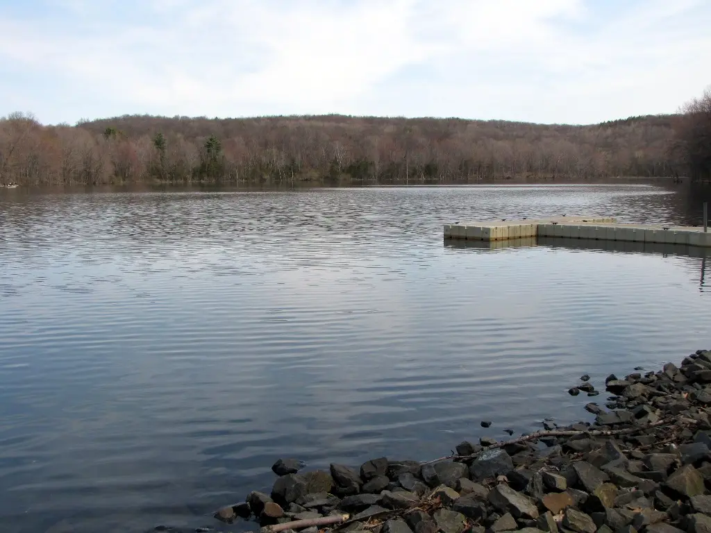 Calm lake with a floating dock and rocky shore under a cloudy sky.