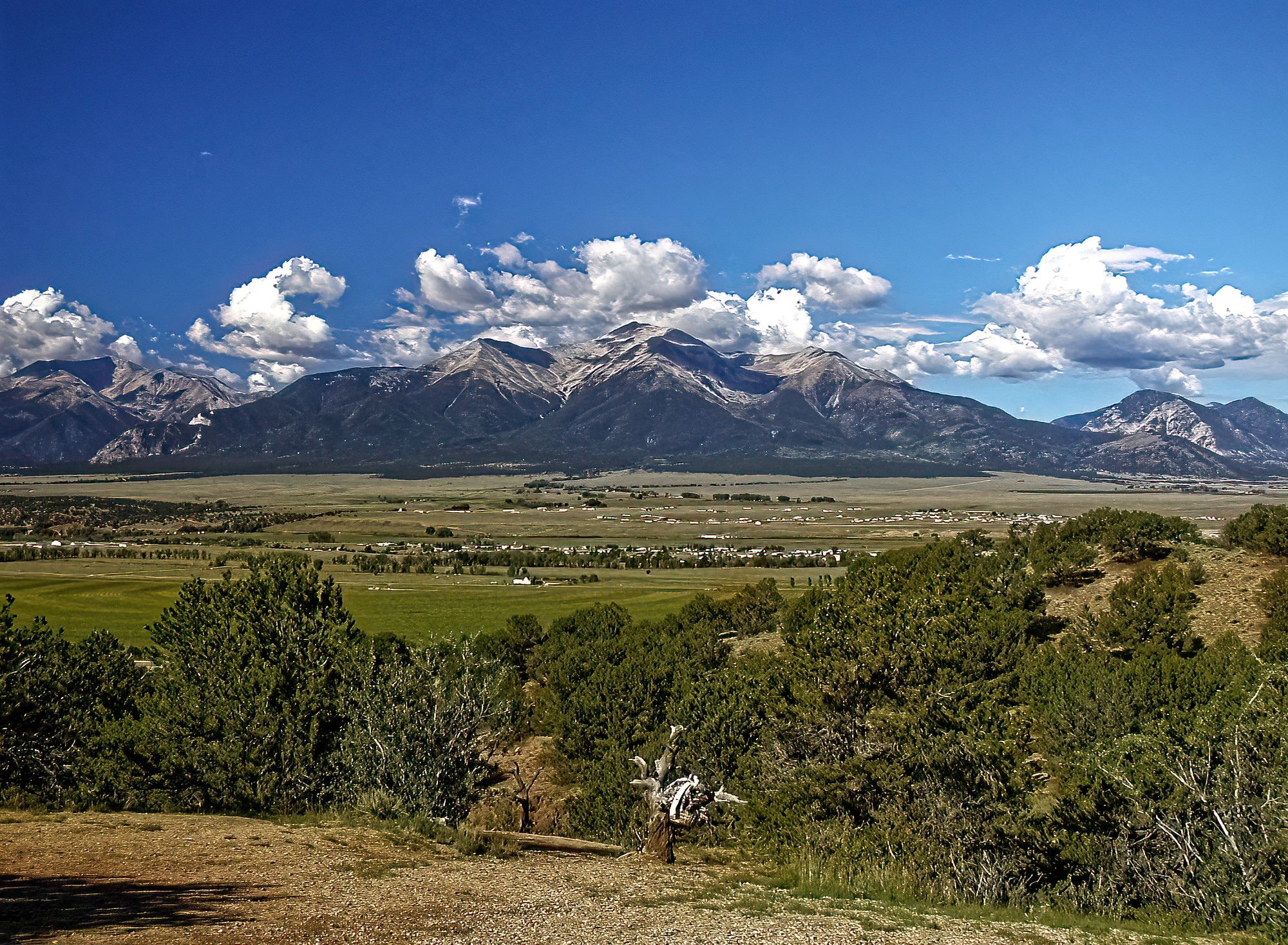 A vast green valley stretches towards majestic mountains under a bright, cloudy sky. - Midland and Broken Boyfriend Trails Loop