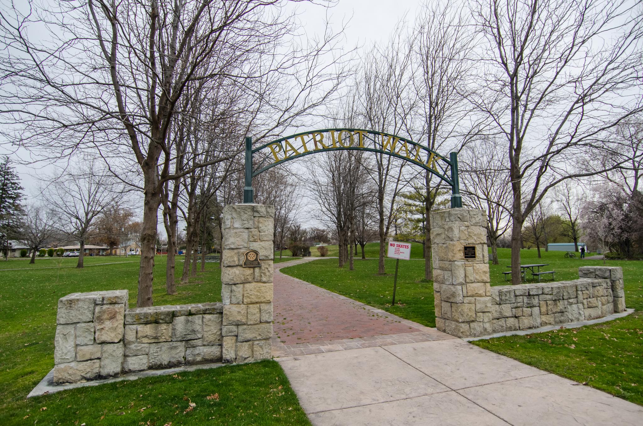 Stone archway entrance to a park with bare trees on an overcast day.
