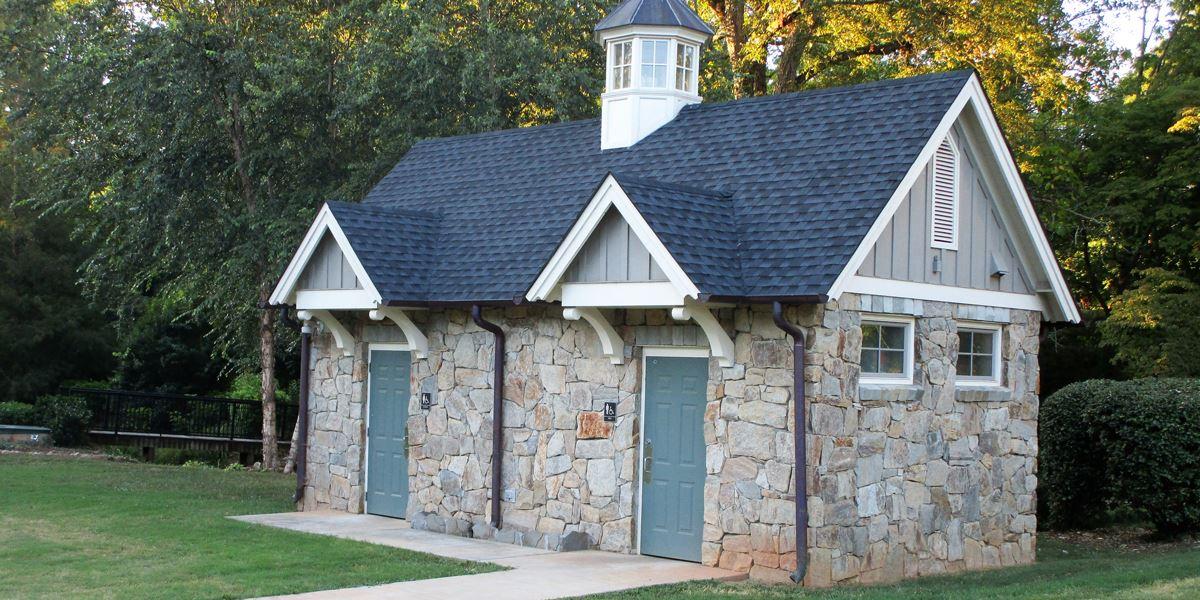 A small stone building with a dark roof and cupola in a grassy park.