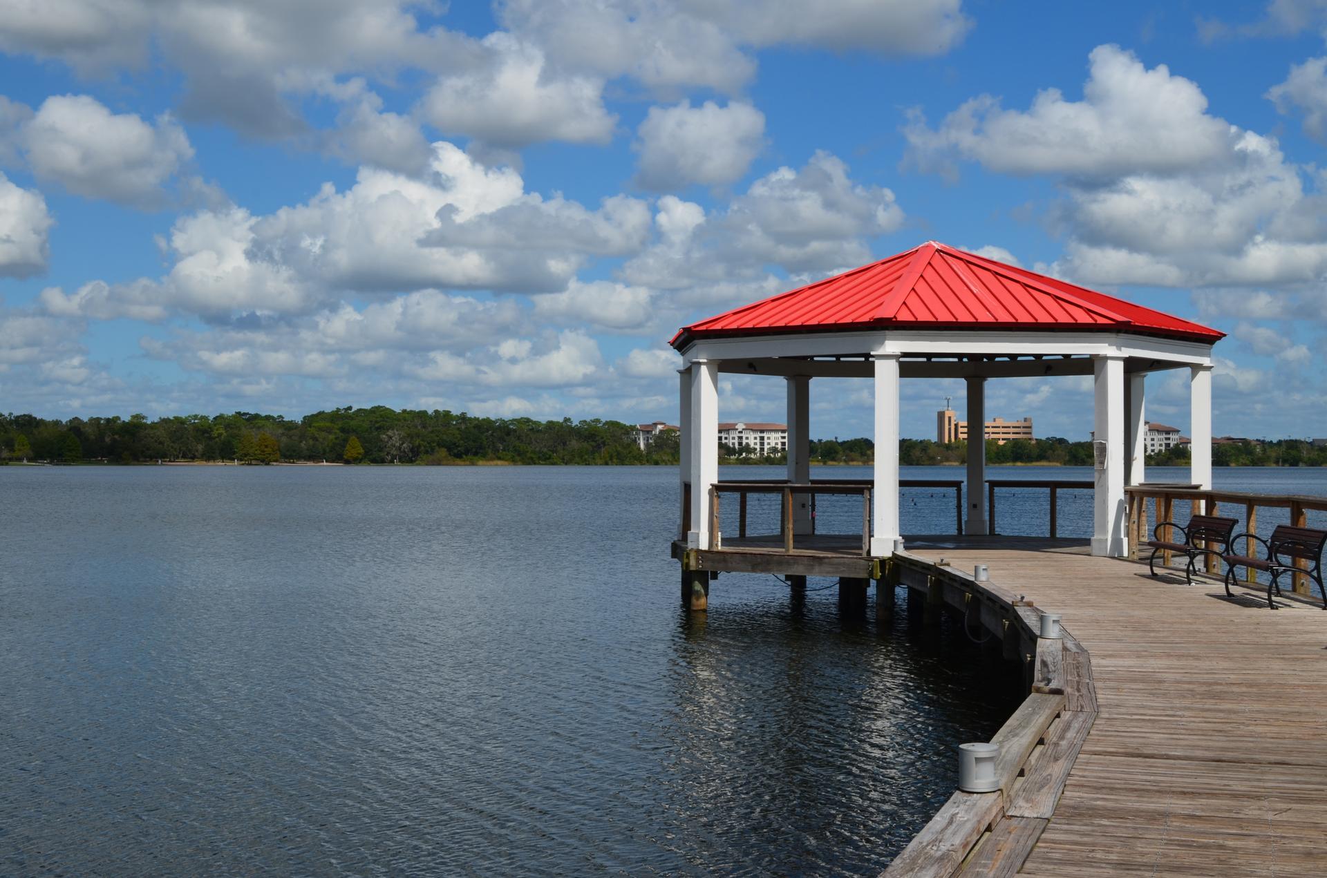 Red-roofed gazebo on a wooden pier extending into a wide lake.