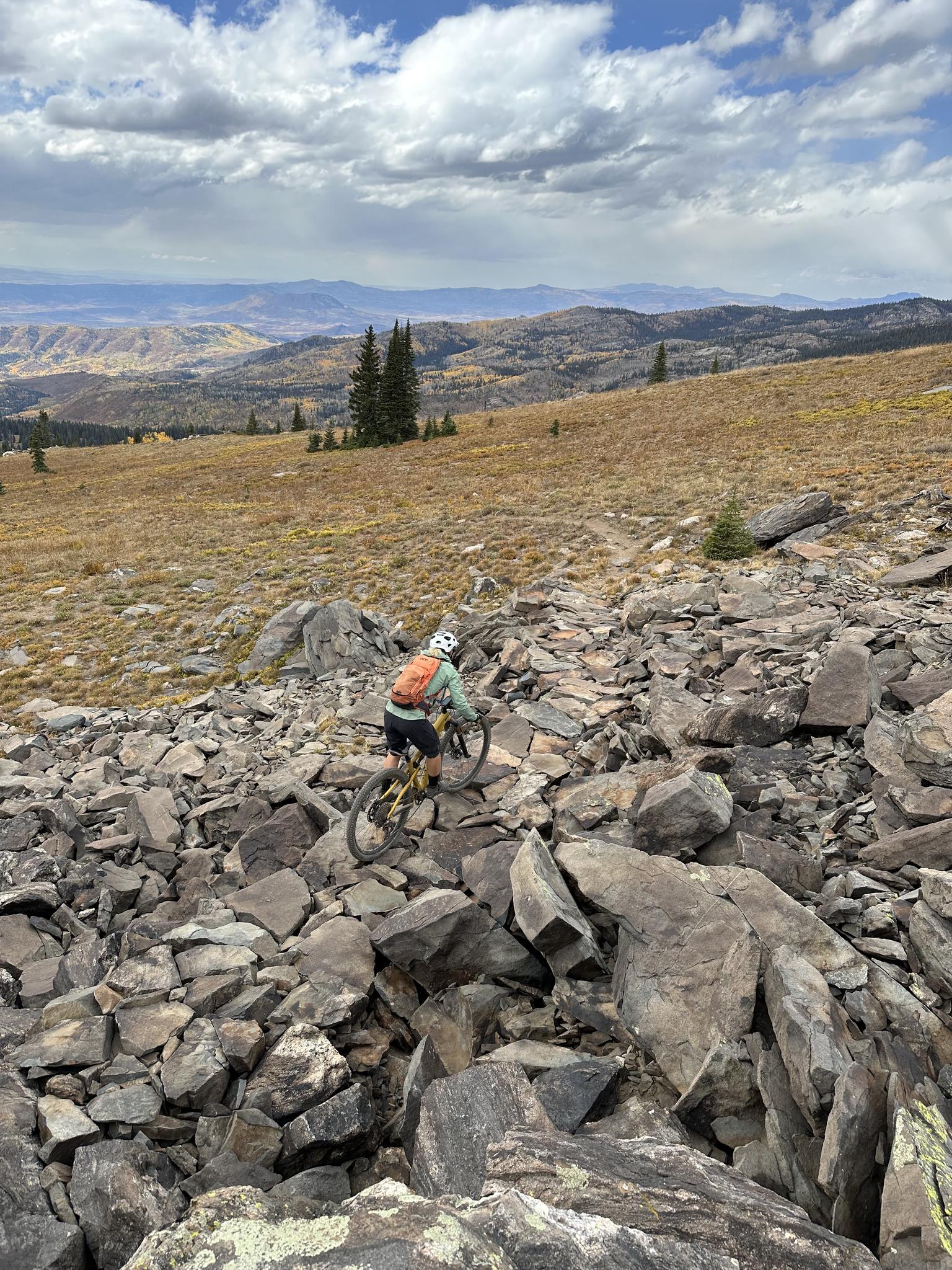 Mountain biker descends a very rocky, barren hillside under cloudy skies.