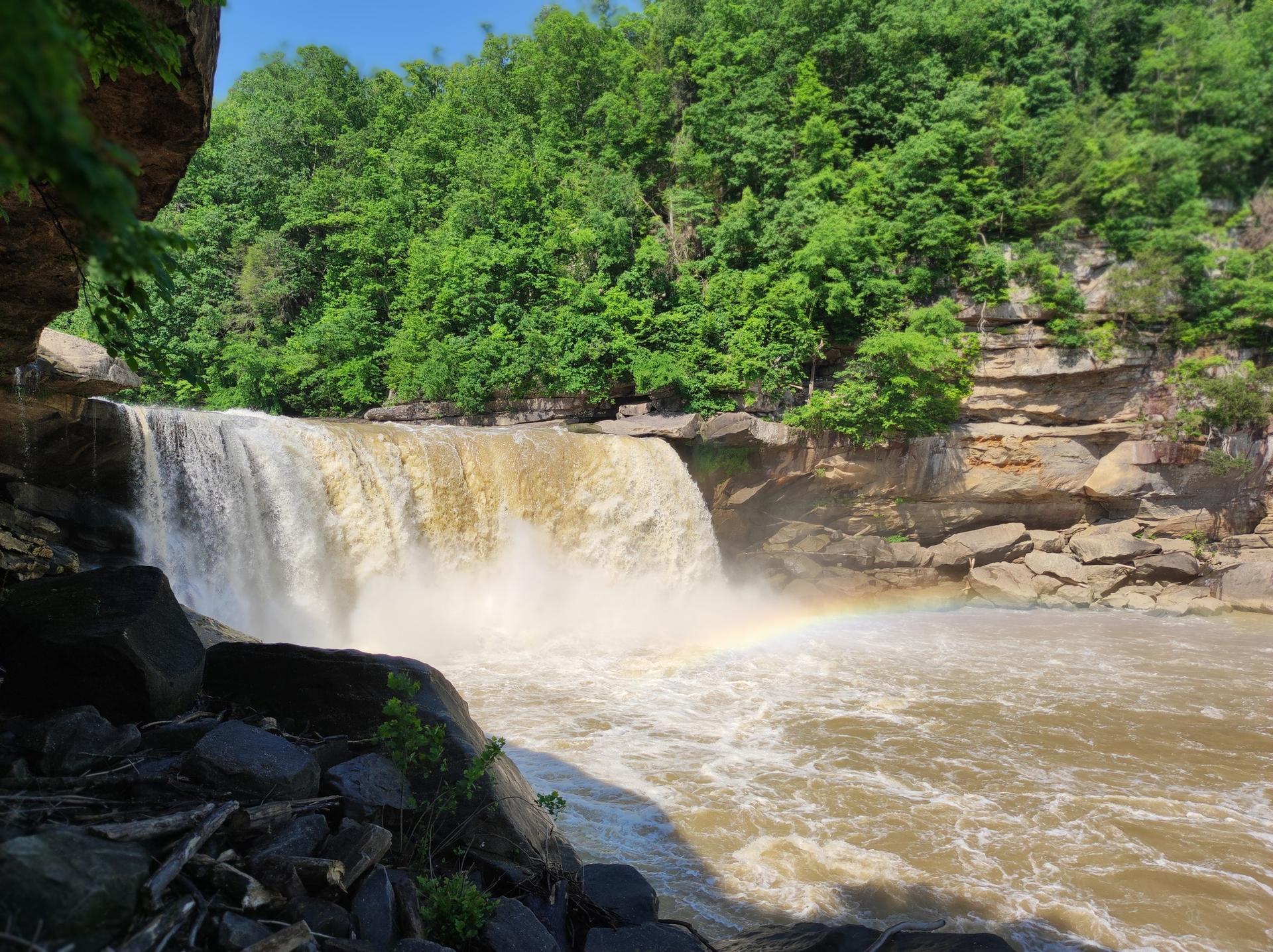 Large, powerful waterfall with a rainbow in the mist, surrounded by green trees.