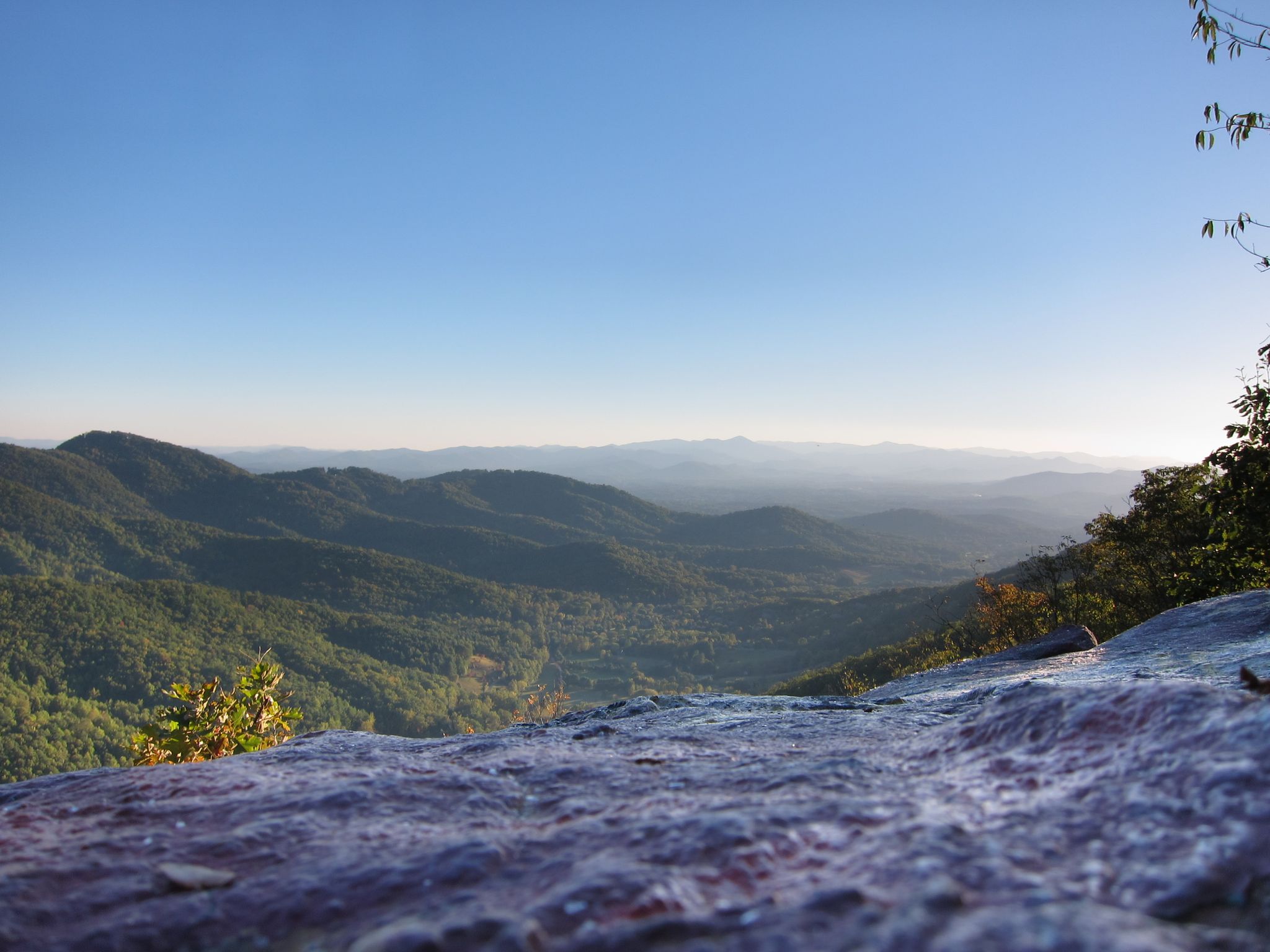 Vast green mountain range under a clear blue sky, with a rocky foreground. - Snowy Pathway in Weaver Park – Elk Mountain view & painted rocks loop from Asheville
